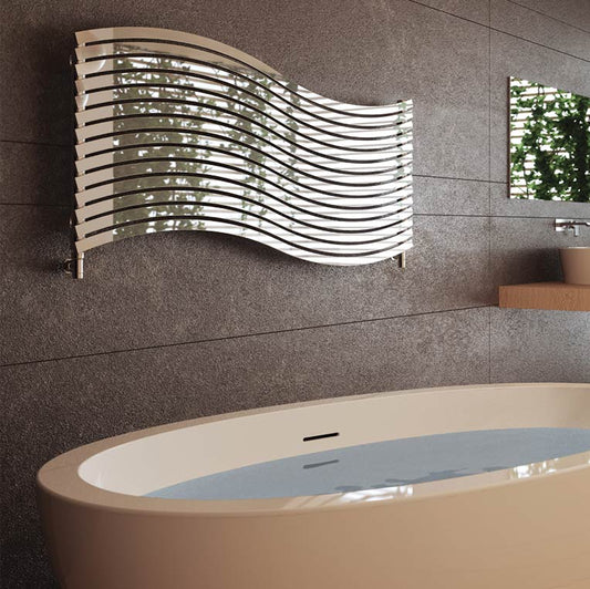Cordivari Lola horizontal designer radiator made of stainless steel, featuring a modern wave-like shape, mounted on a bathroom wall above a bathtub and surrounded by plants.