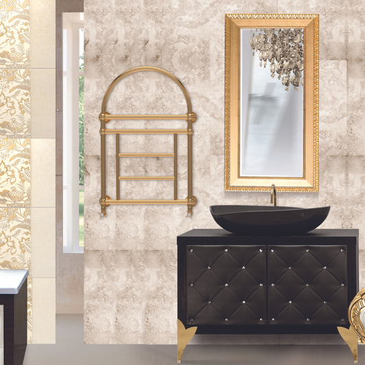 Elegant retro-style hot water towel warmer with a curved top rail, in an antique gold finish, mounted on a wall beside a black vanity with gold accents.