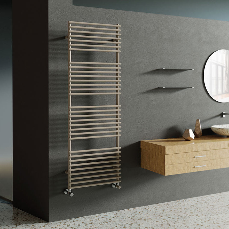 A vertical hot water towel warmer in a painted mild steel color, positioned next to a wooden vanity with a sink and a round mirror on the wall.