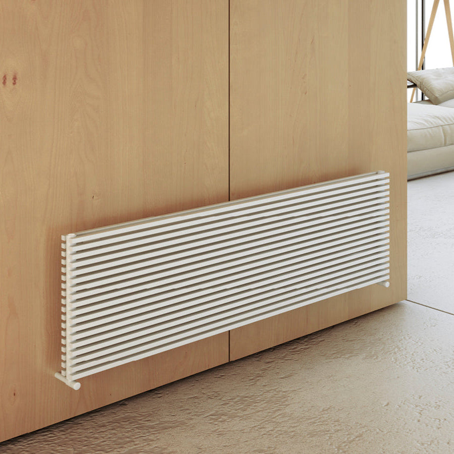 A horizontal hot water radiator with vertical collectors, painted in white color, mounted on a wooden wall.